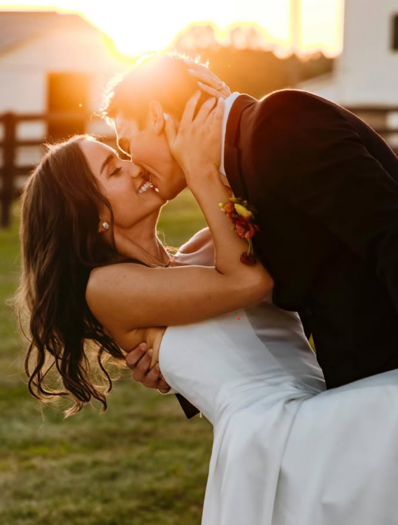 Wedding couple kissing in a sunlit field during golden hour
