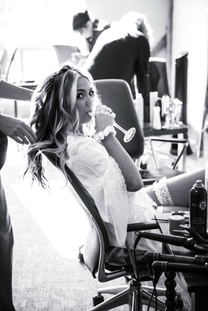 Bride getting ready with champagne while having her hair styled