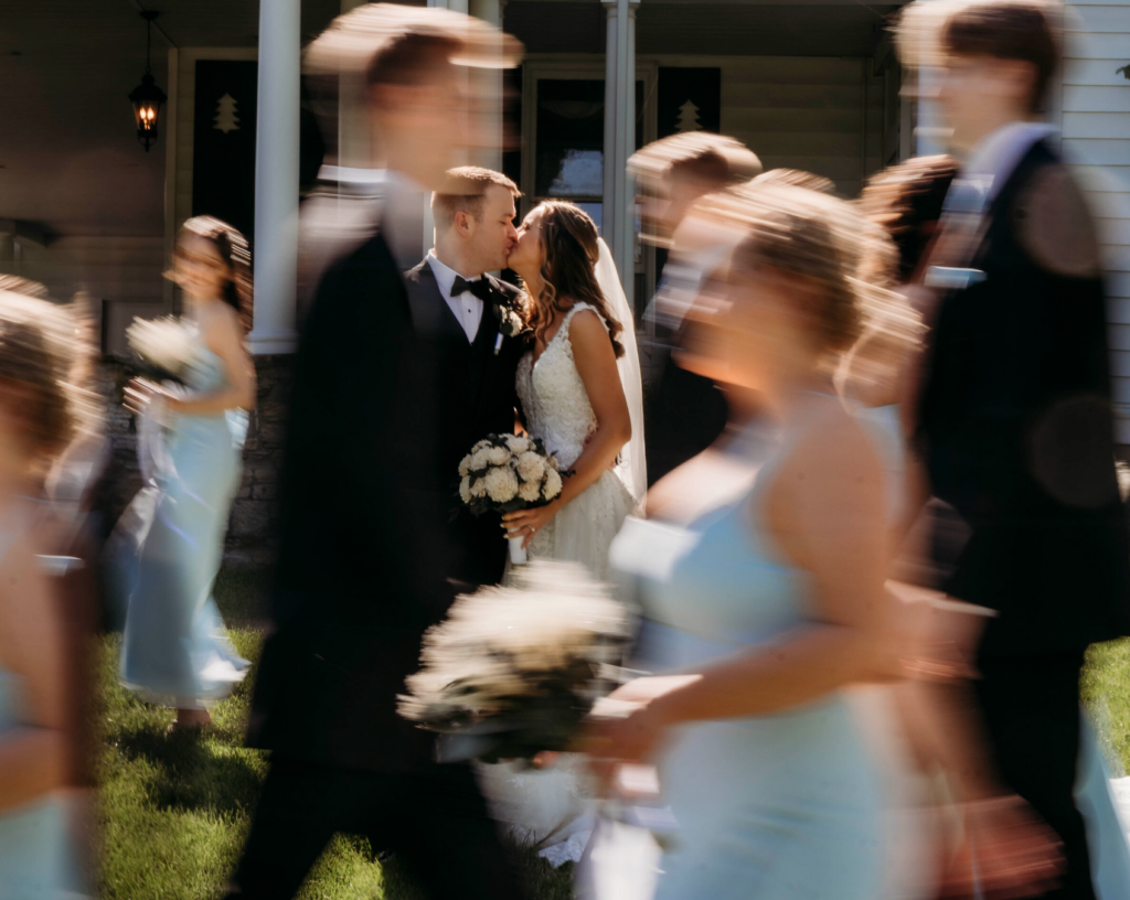 Artistic wedding portrait of bride and groom kissing with guests passing by