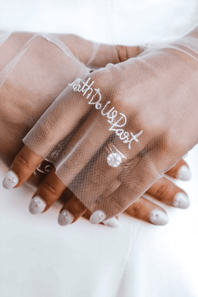 Detail photograph of bride wearing embroidered mesh gloves with wedding ring
