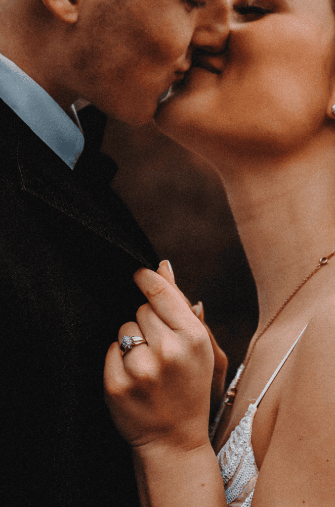 couple shares a kiss during a close up shot of the engagement ring
