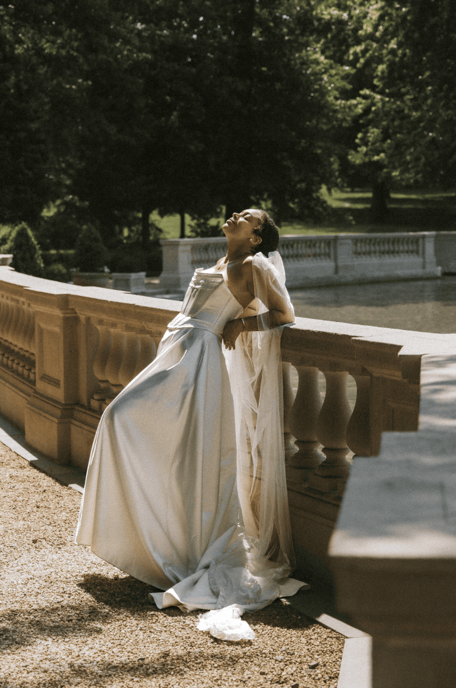 Bride in wedding dress leaning back against a railing on her wedding day.