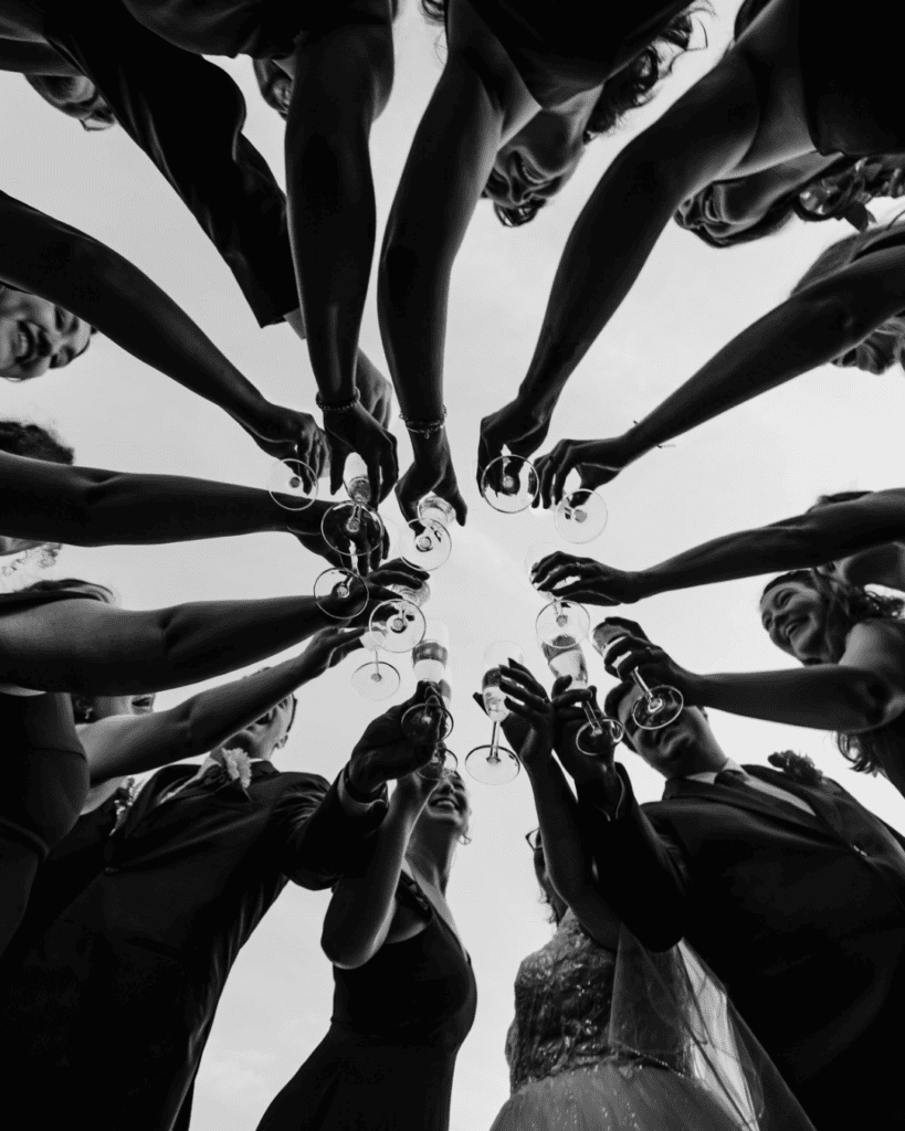 Wedding guests raising champagne glasses in a celebratory toast, photographed from below.
